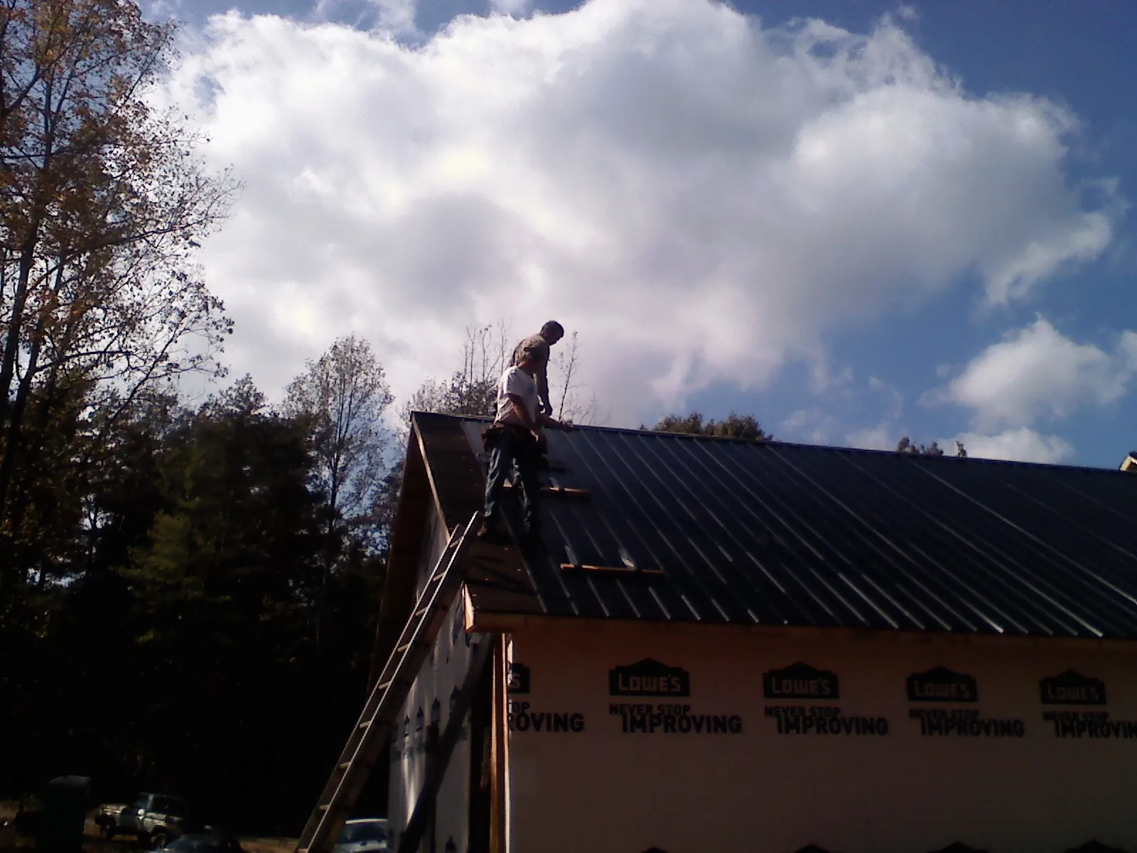 Roofer fastening dark metal panels high against a cloudy sky, from a Roof Inspection job in Adrian